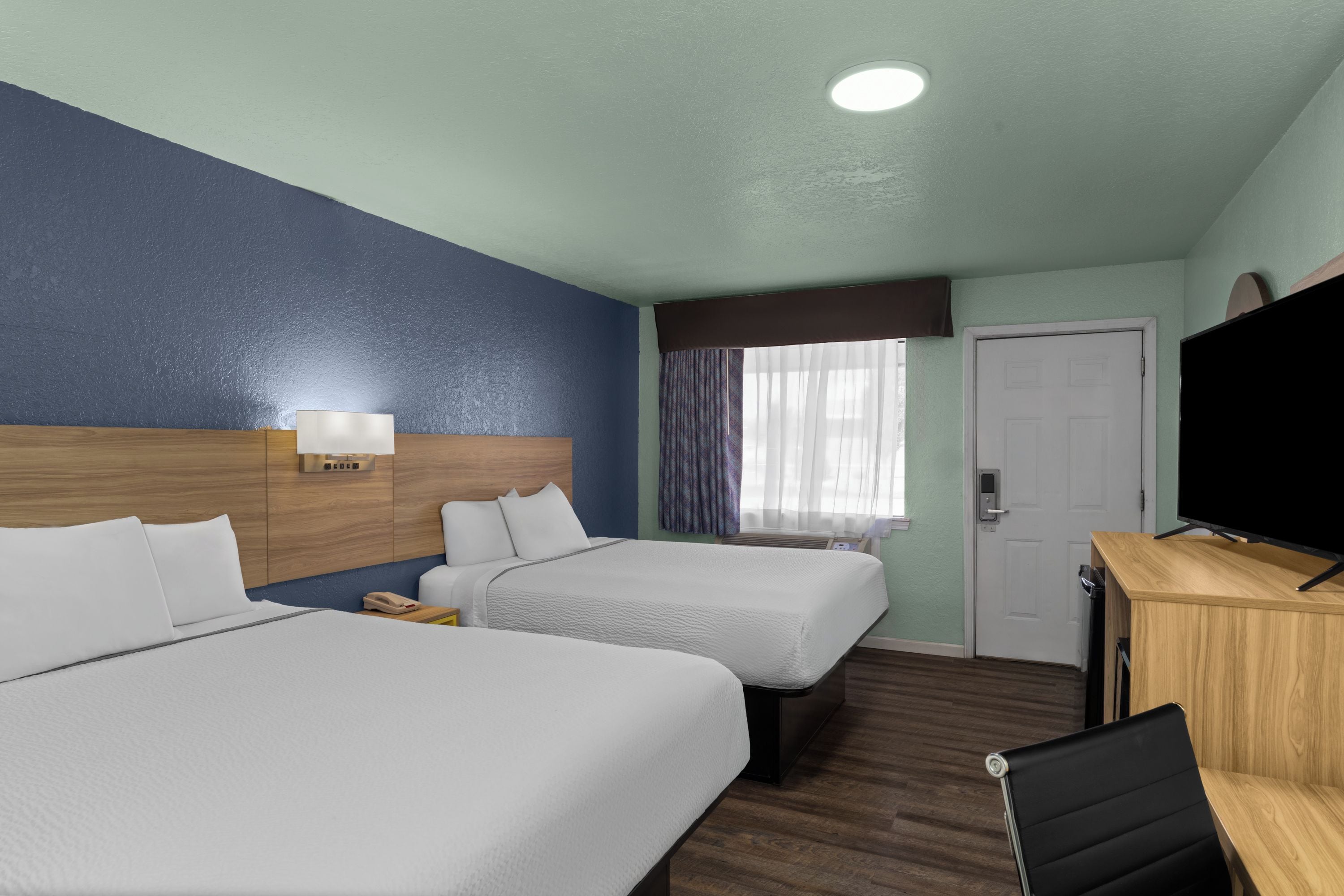 A hotel room with two beds, a desk with a television, and a window with curtains.