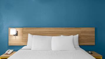 Habitación de hotel con cabecera de madera, cama blanca, mesita de noche con teléfono y luz de pared.