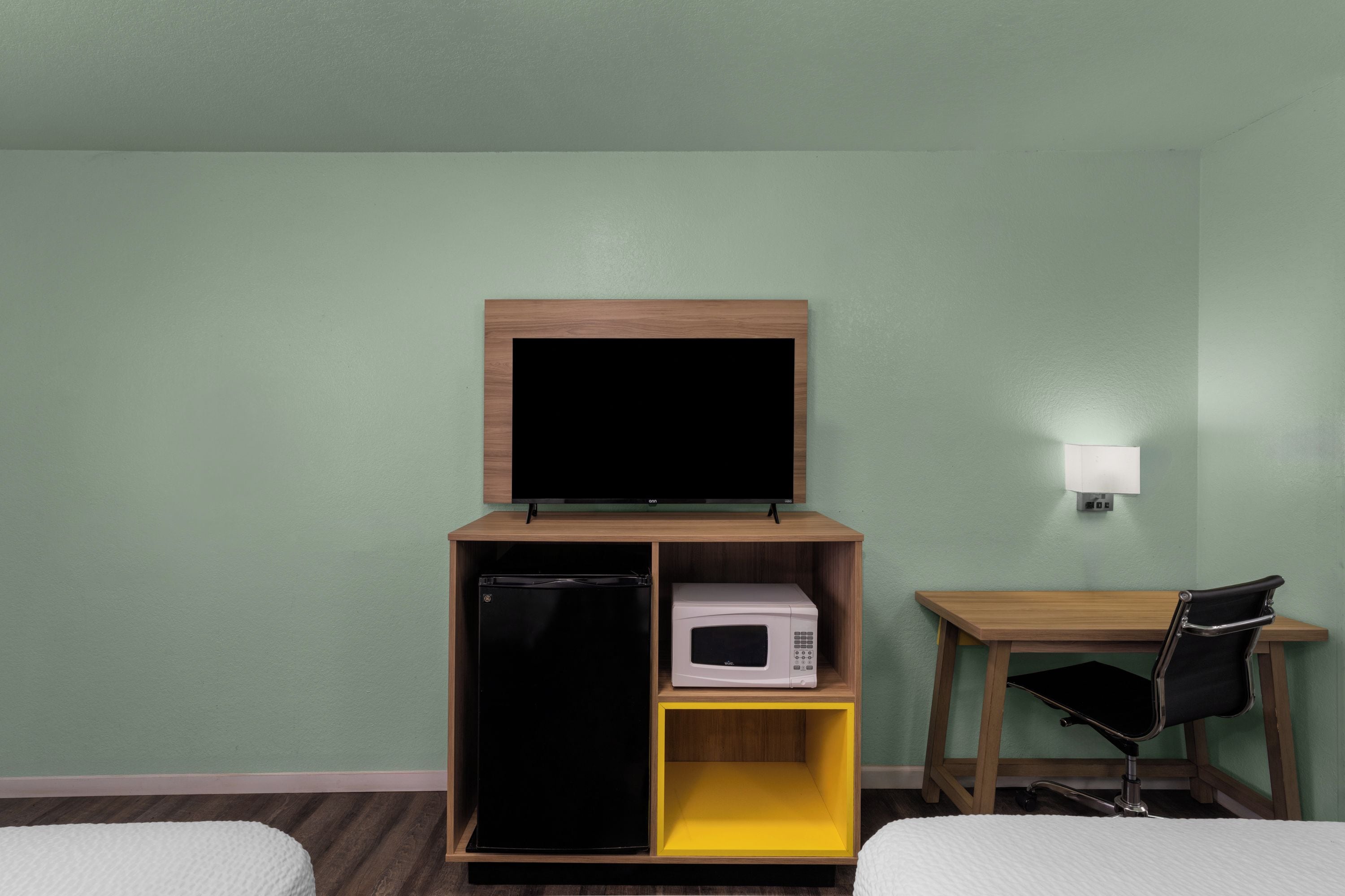A hotel room with a bed, a desk with a chair, a television, a refrigerator, and a microwave.