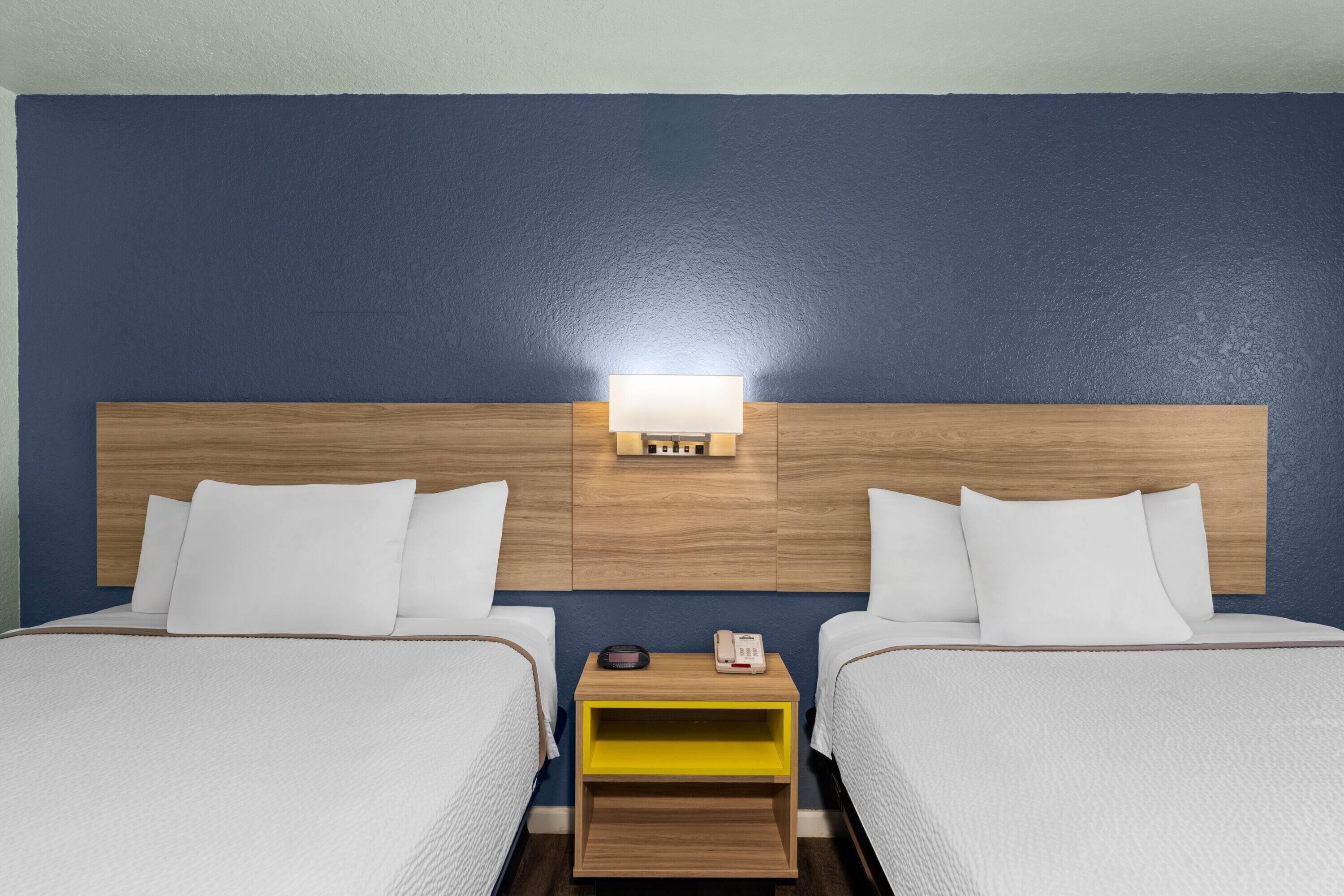 A hotel room with two beds, a nightstand with a lamp, and a wall-mounted telephone.