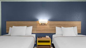 A hotel room with two beds, a nightstand with a lamp, and a wall-mounted telephone.