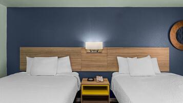 Een hotelkamer met twee bedden, een houten hoofdeinde, een nachtkastje met een telefoon en een wandlamp.