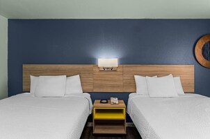 A hotel room with two beds, a wooden headboard, a bedside table with a phone, and a wall-mounted light.