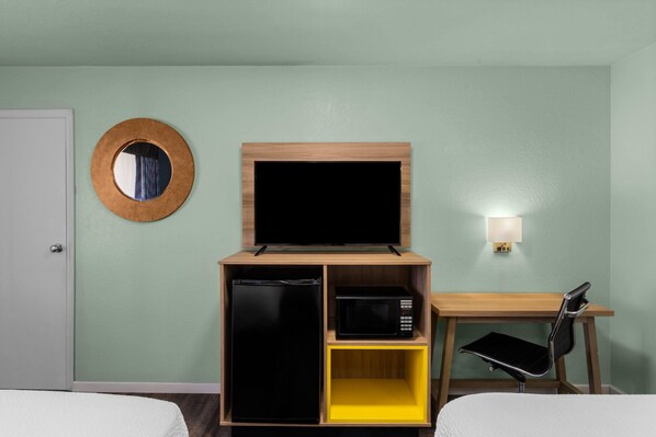 Habitación de hotel con cama, escritorio, televisor, microondas y refrigerador pequeño.