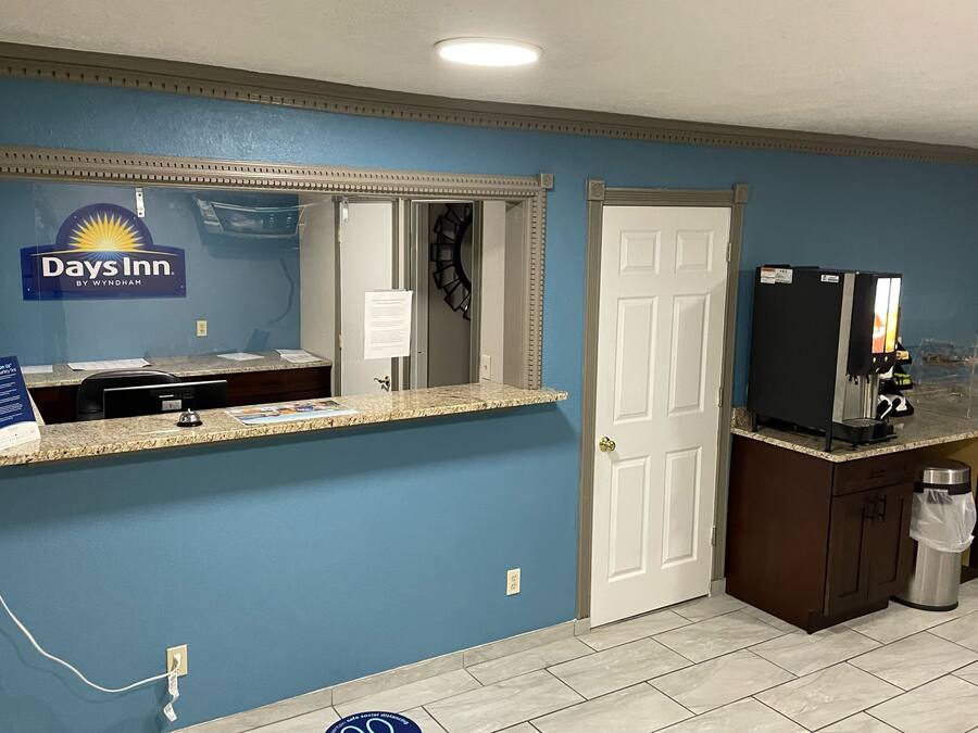 Una zona de recepción con el letrero de Days Inn, un mostrador con caja registradora, una cafetera y un cubo de basura.