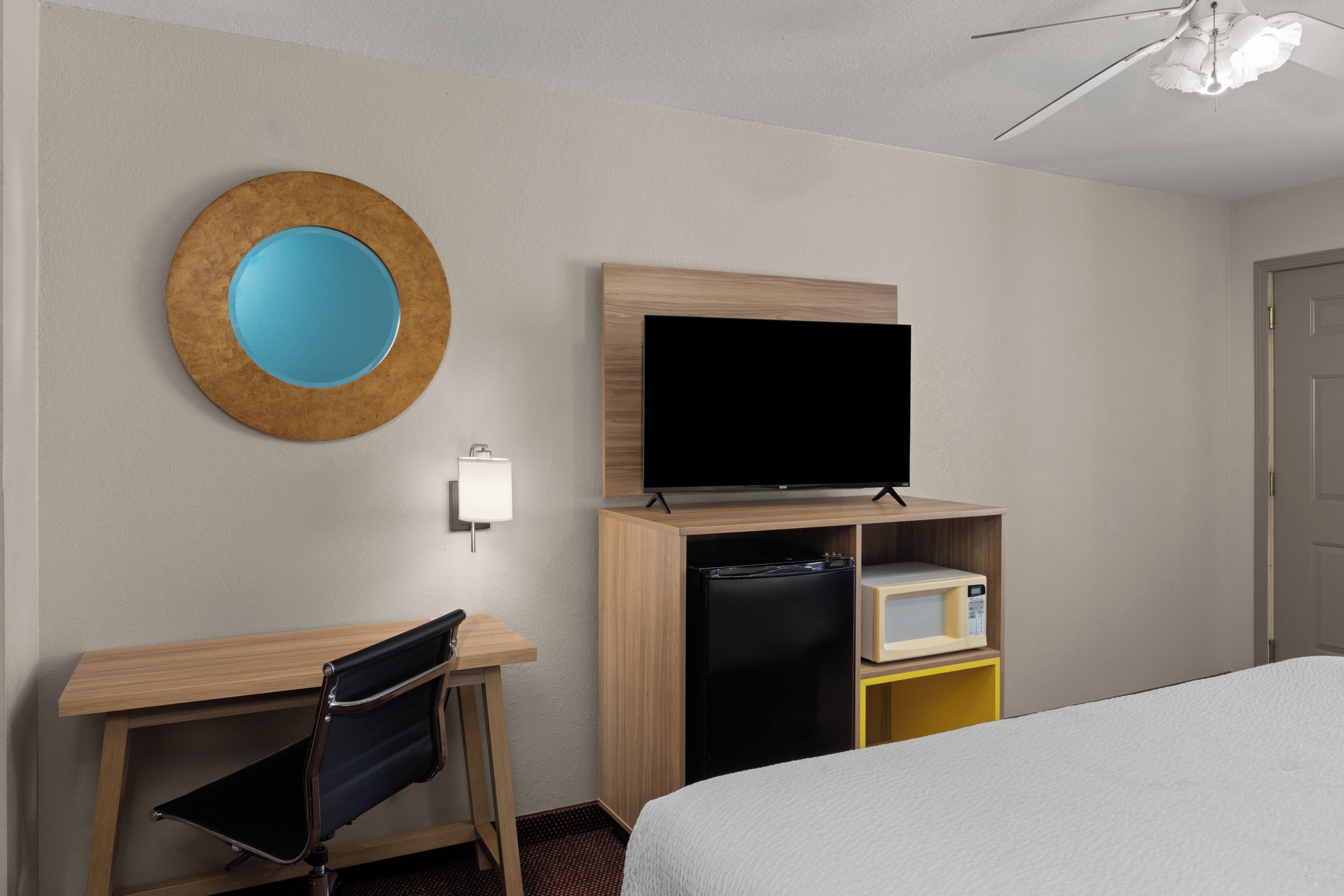 A hotel room with a bed, a desk with a chair, a television, a refrigerator, and a microwave.
