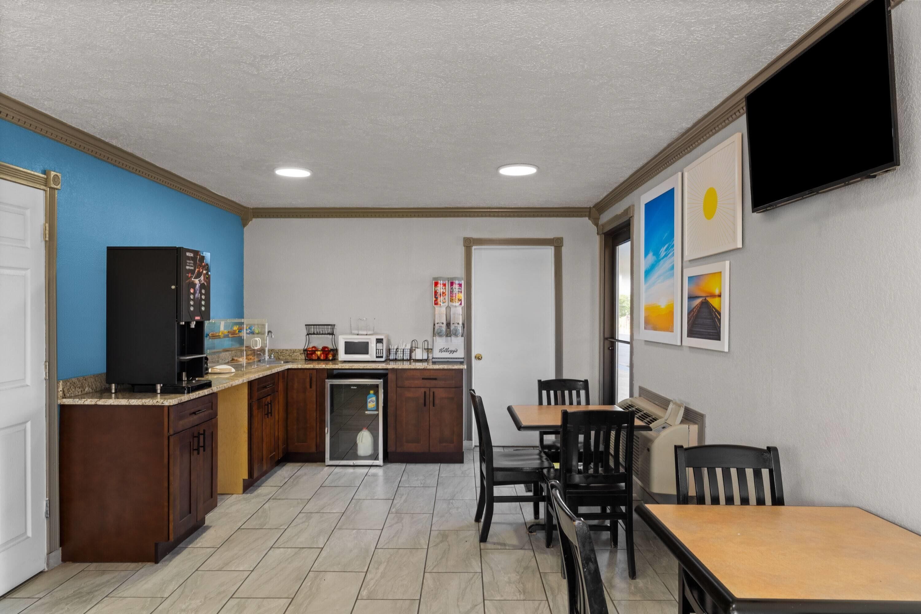 A compact kitchen with a microwave, coffee maker, and a refrigerator. There is a dining area with a table and chairs.
