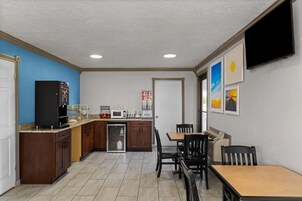 Cocina compacta equipada con microondas, cafetera y refrigerador. Hay un comedor con mesa y sillas.