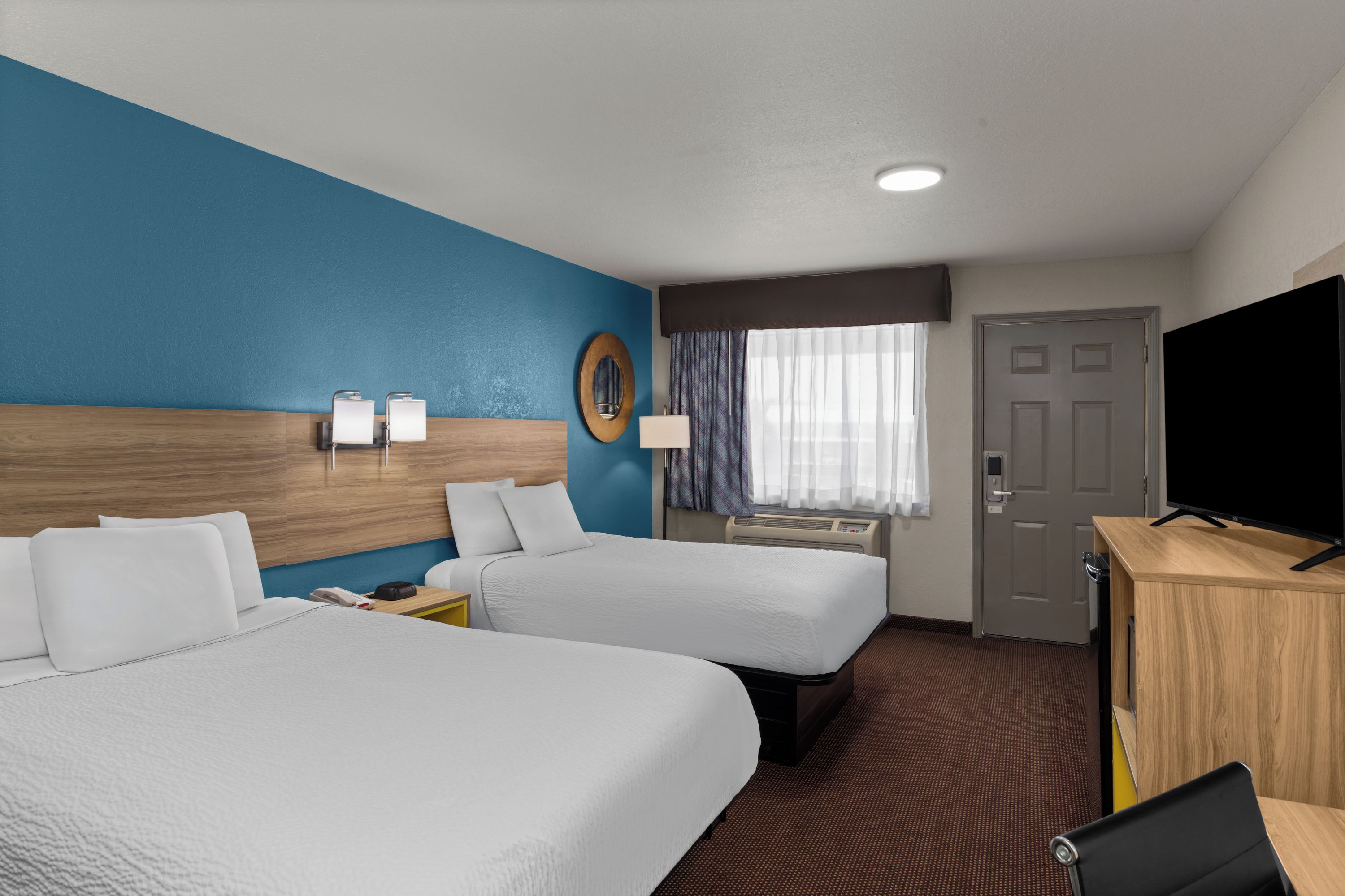 A hotel room with two beds, a desk, a television, a mirror, and a window with curtains.