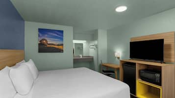 A hotel room with a bed, a television, a desk, and a bathroom visible through an open door.