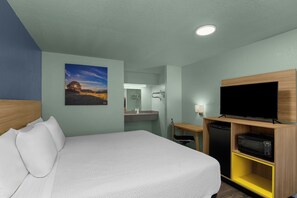 Habitación de hotel con cama, televisión, escritorio y baño visible a través de una puerta abierta.