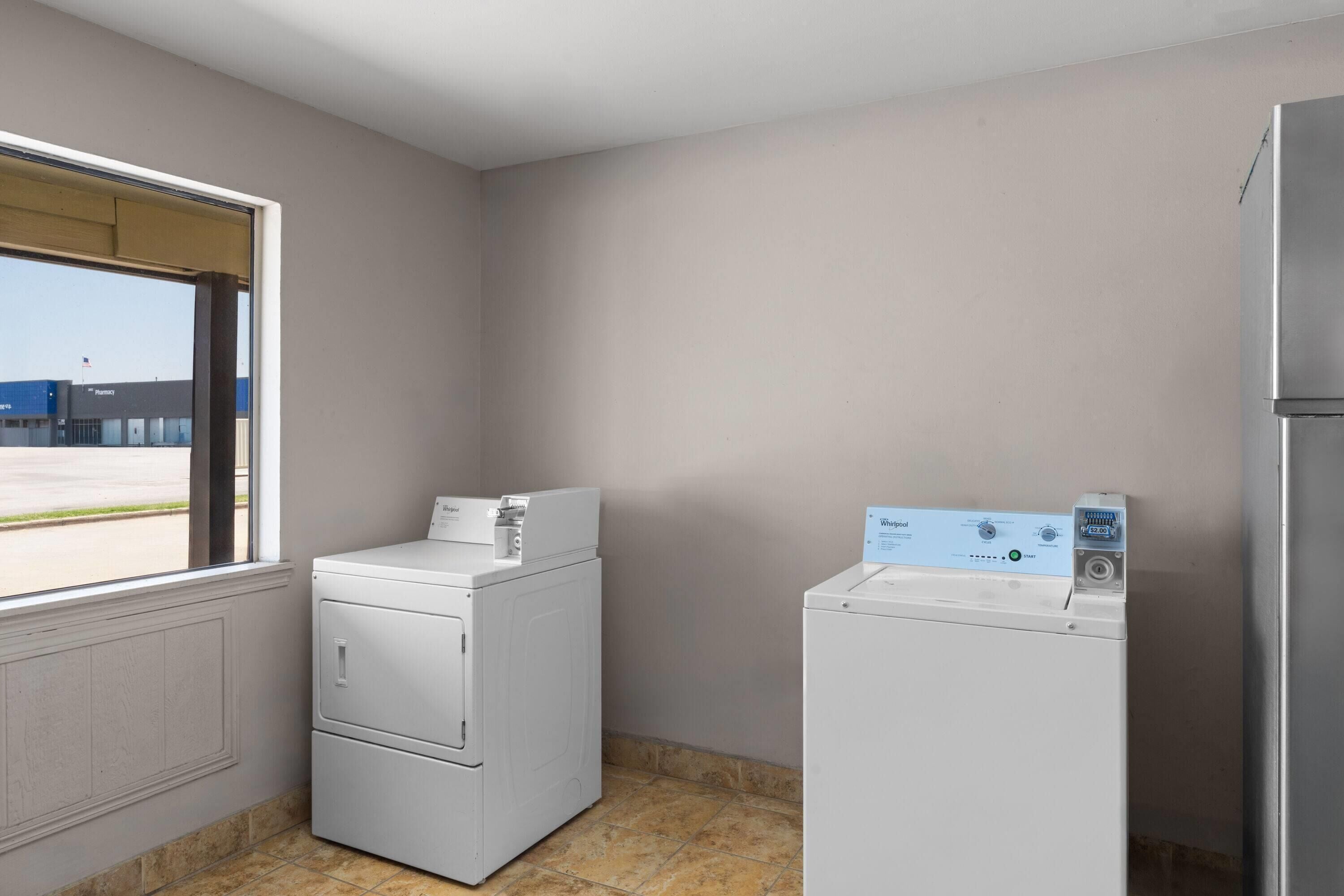 A laundry room with two front-loading washers and dryers, a window with a view of a pharmacy, and a tiled floor.