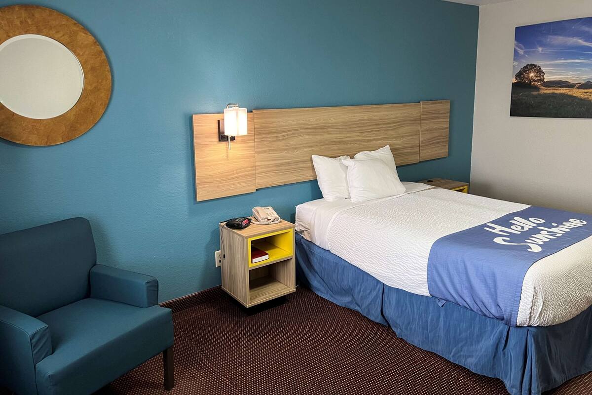 A hotel room with a bed, a nightstand with a phone, a chair, and a wall-mounted mirror.