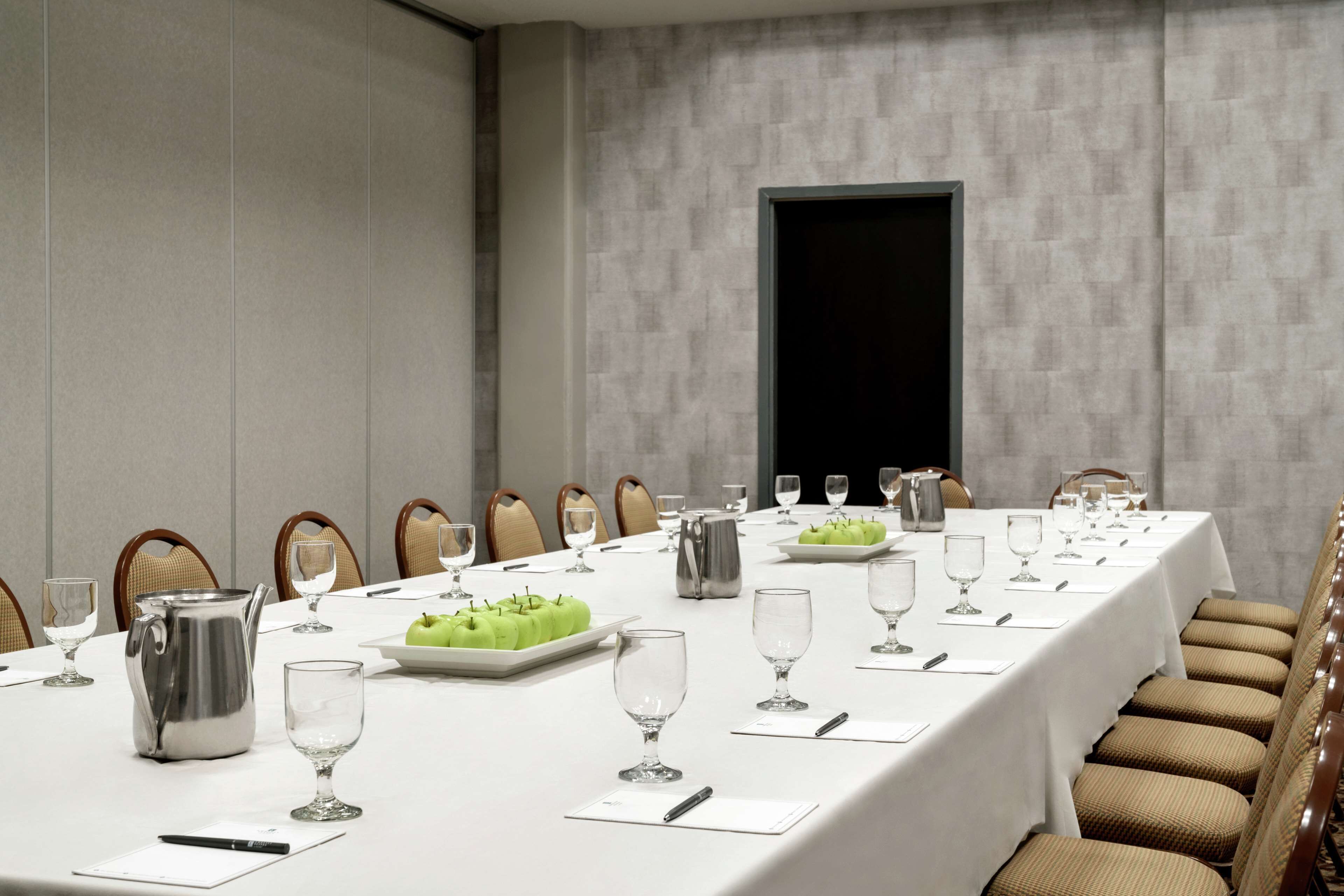 A conference room with a long table set for a meeting, equipped with chairs, a coffee pot, and a fruit platter.
