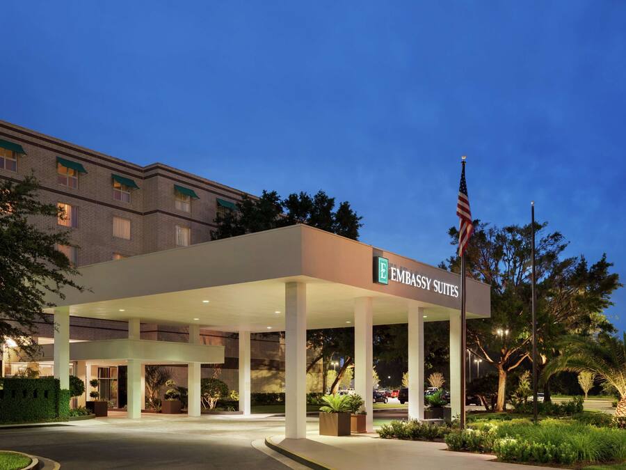 A hotel entrance with a covered area, an American flag, and a sign reading "Embassy Suites".