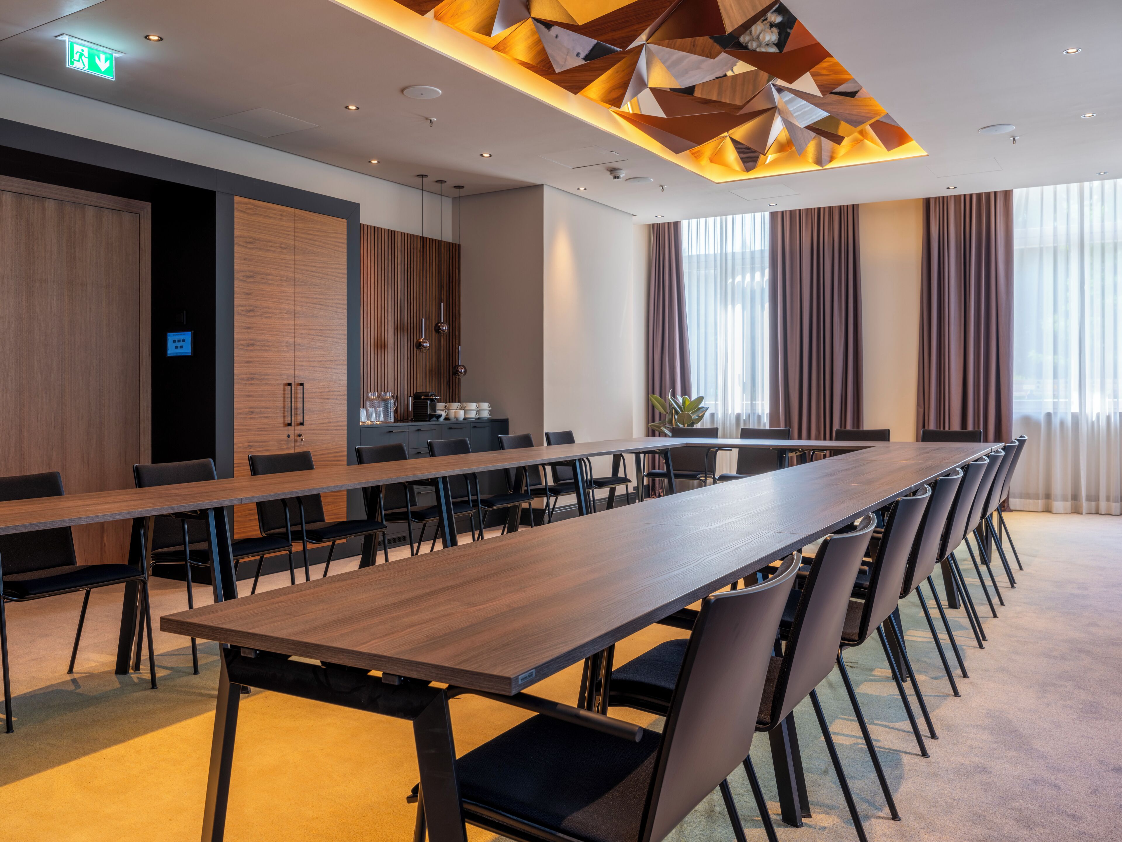 Ein Konferenzraum mit langem Tisch, Stühlen, einer kleinen Küchenzeile und einem großen Fenster mit Vorhängen.