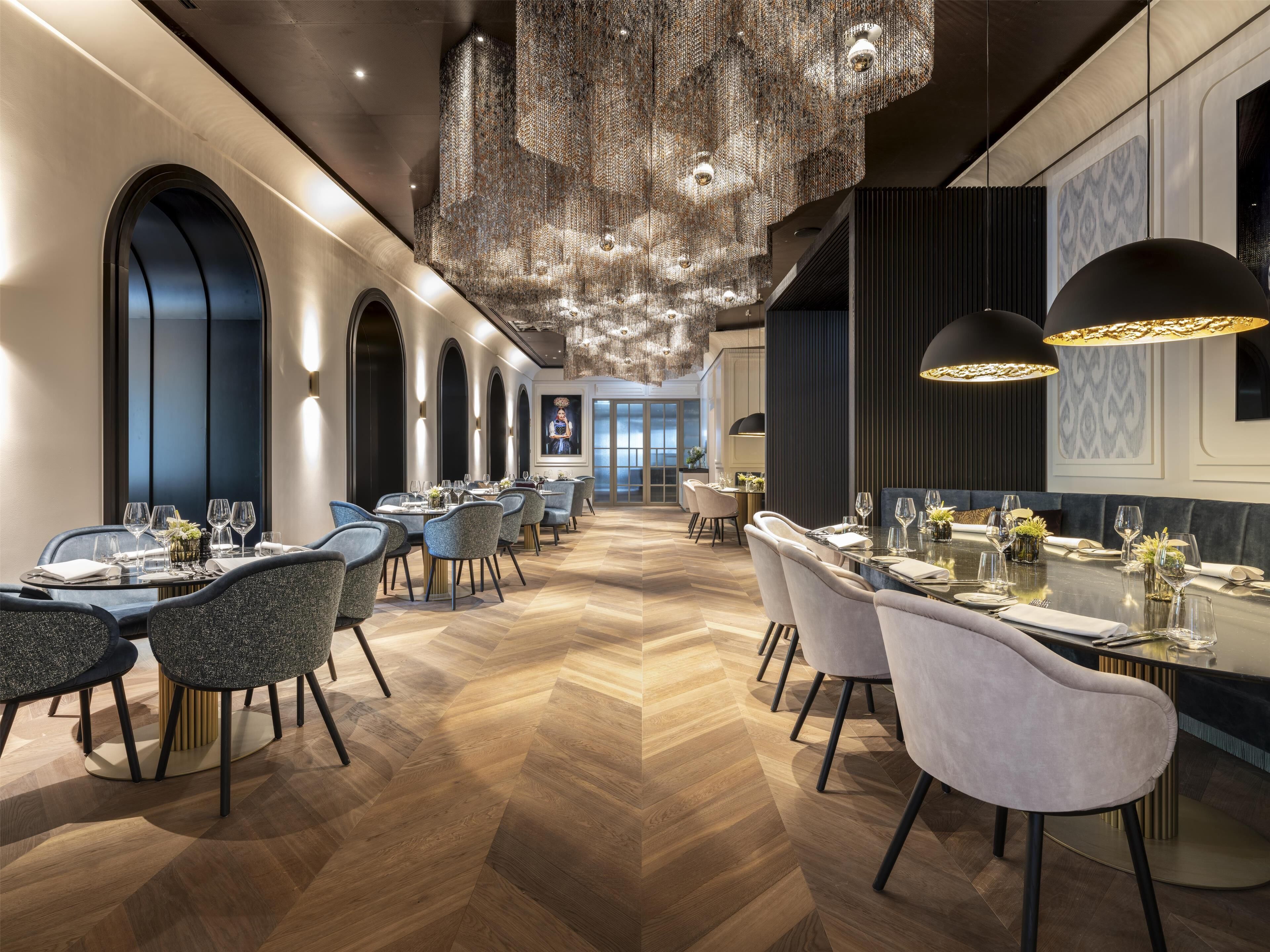 A modern dining area with multiple tables, chairs, and a decorative chandelier.