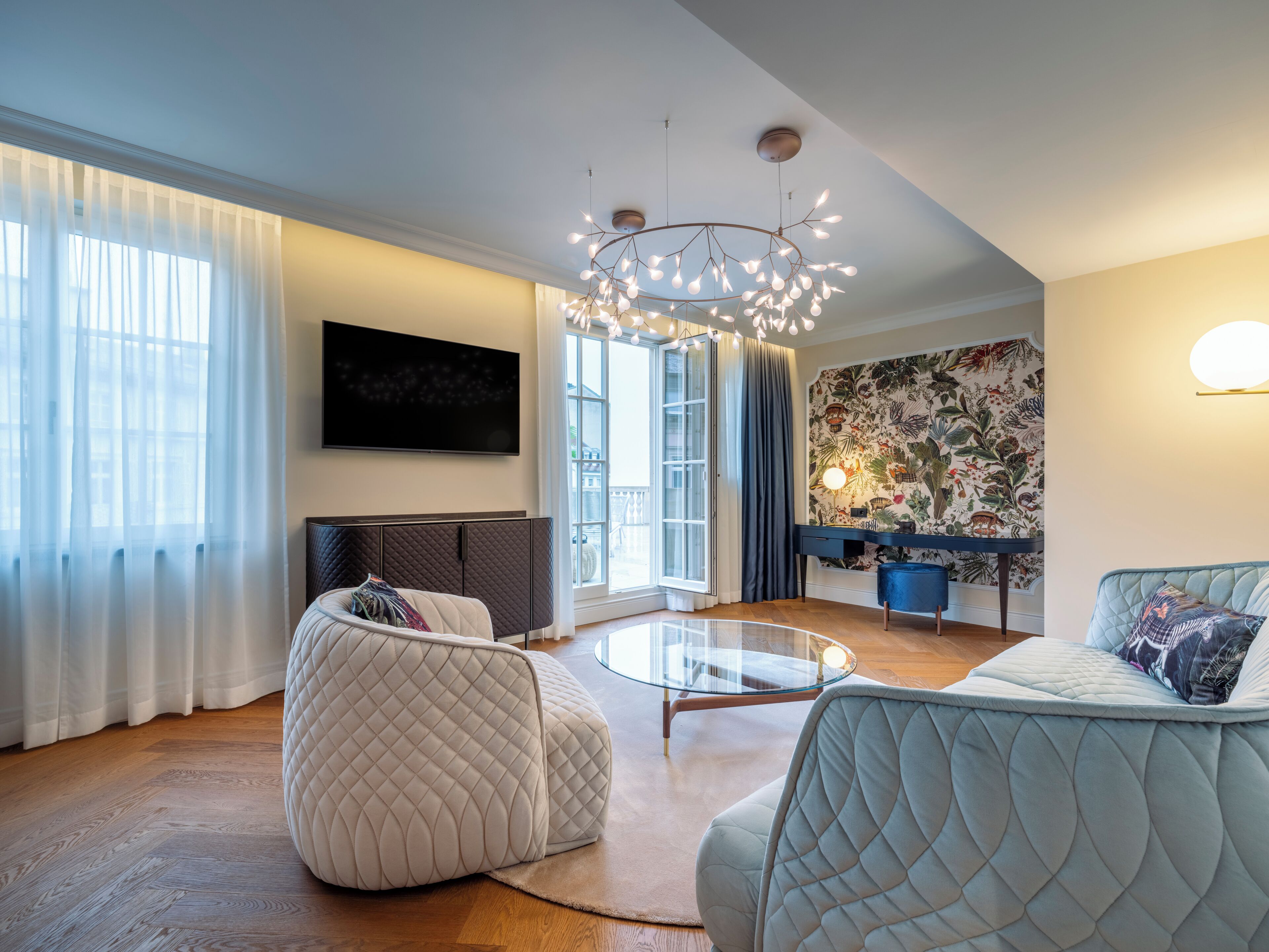 Ein modernes Wohnzimmer mit einem Glastisch, einer Couch, einem Fernseher und einer dekorativen Leuchte.