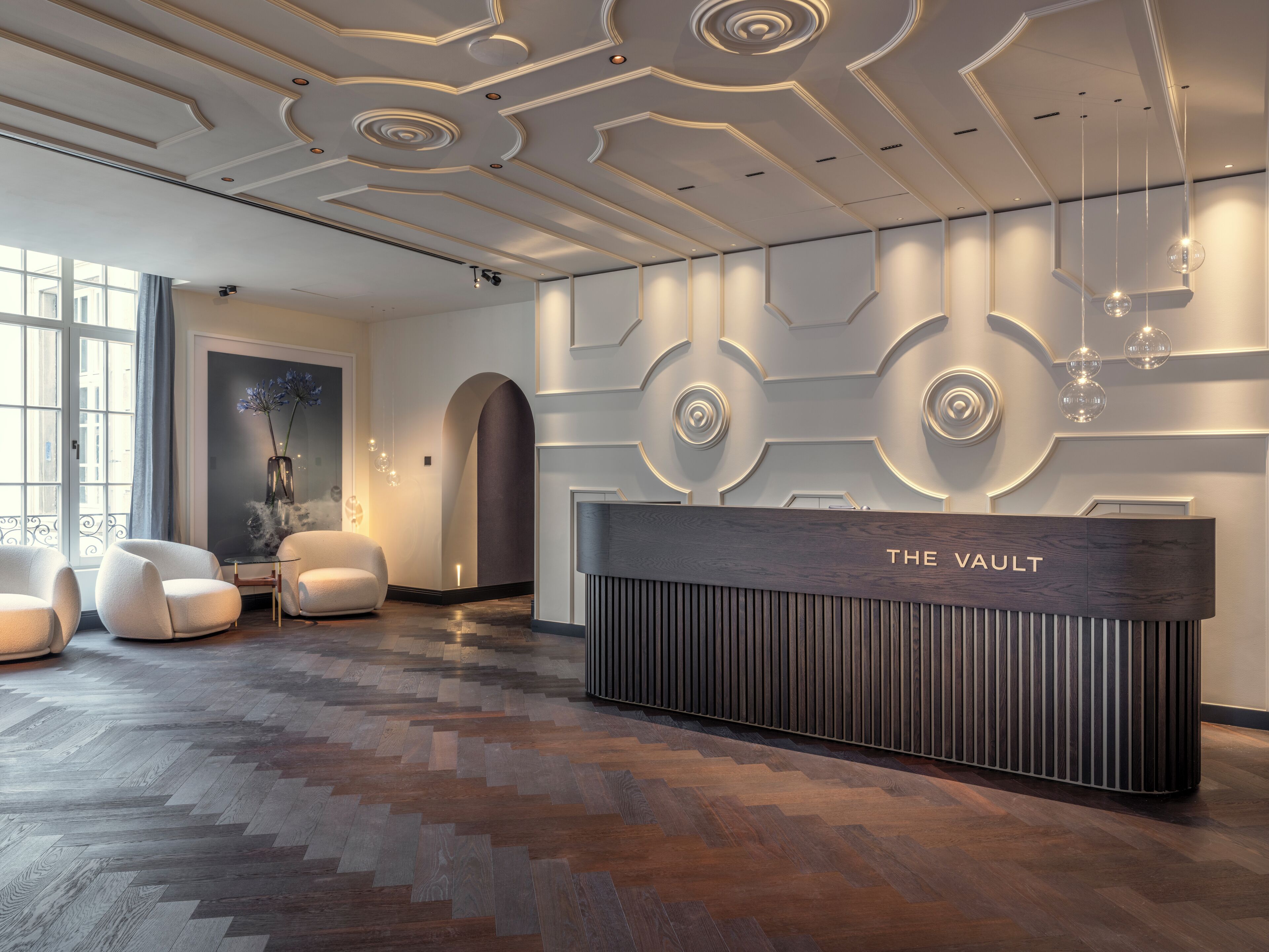 Un espace d’accueil au design moderne, comprenant un comptoir en bois portant l’inscription « THE VAULT » et un sol orné d’un motif en chevrons.