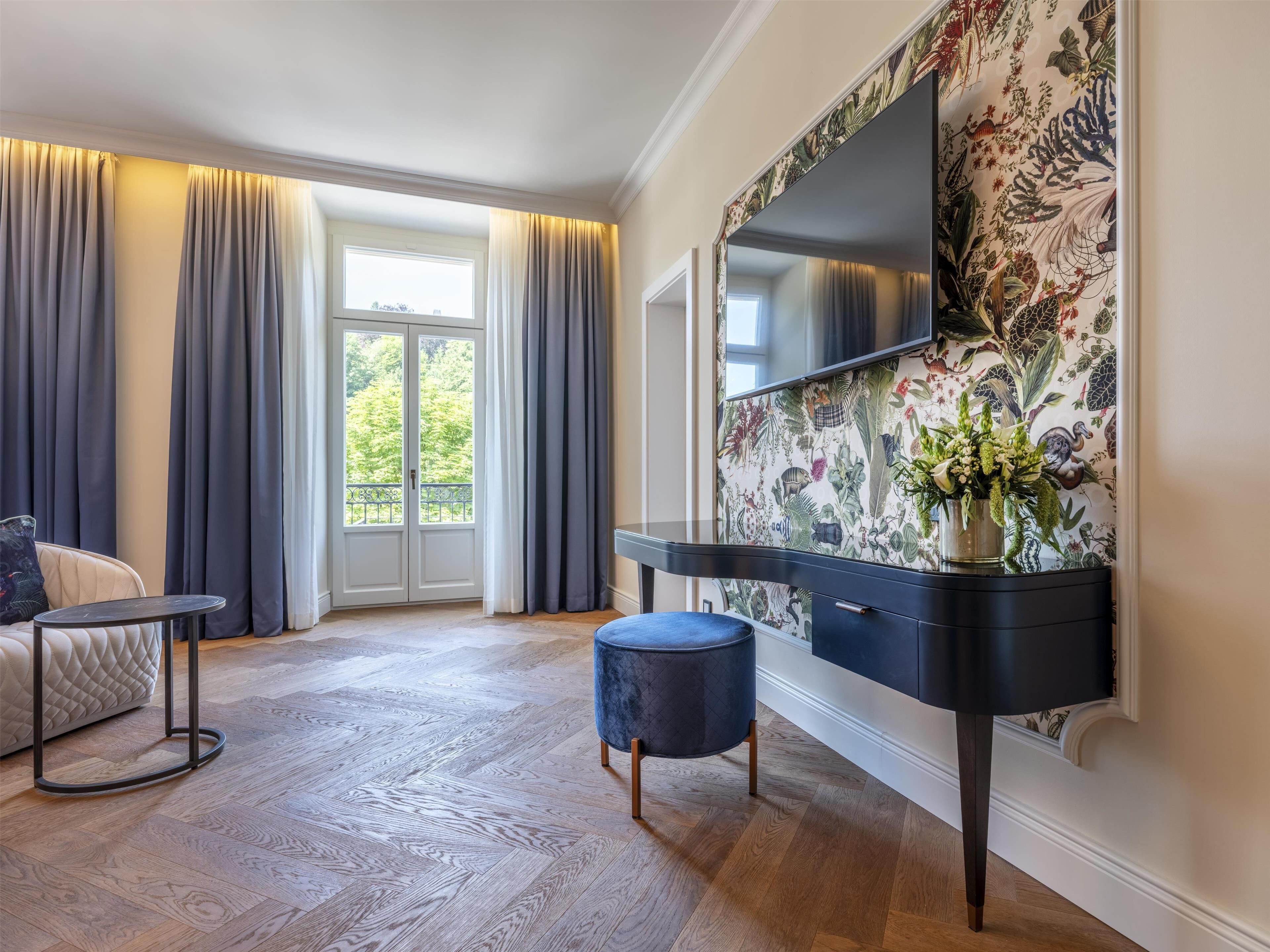 Una habitación de hotel moderna con un ventanal grande, un televisor de pantalla plana, una consola oscura y un papel tapiz estampado.