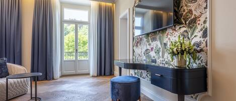 A modern hotel room with a large window, a flat-screen TV, a dark console table, and a patterned wallpaper.
