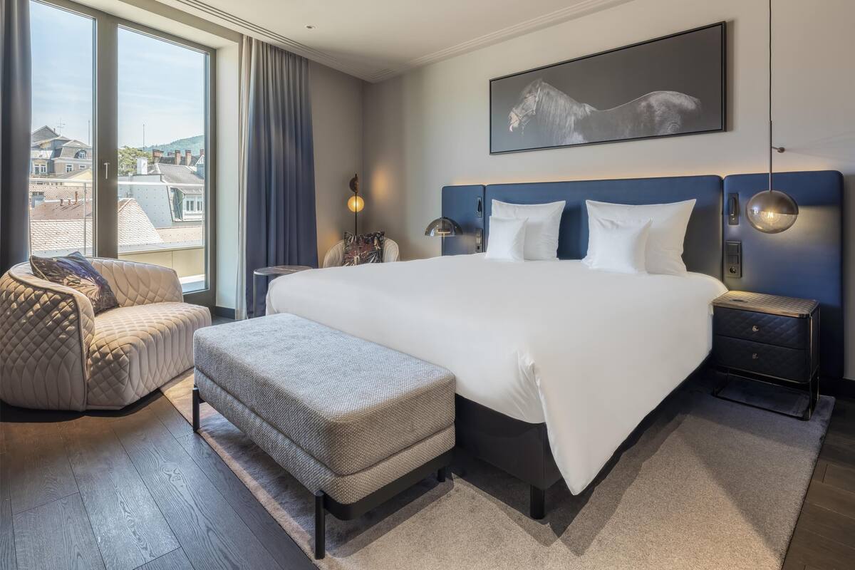 Une chambre d’hôtel moderne avec un grand lit, un canapé, une petite table et une vue sur la ville.