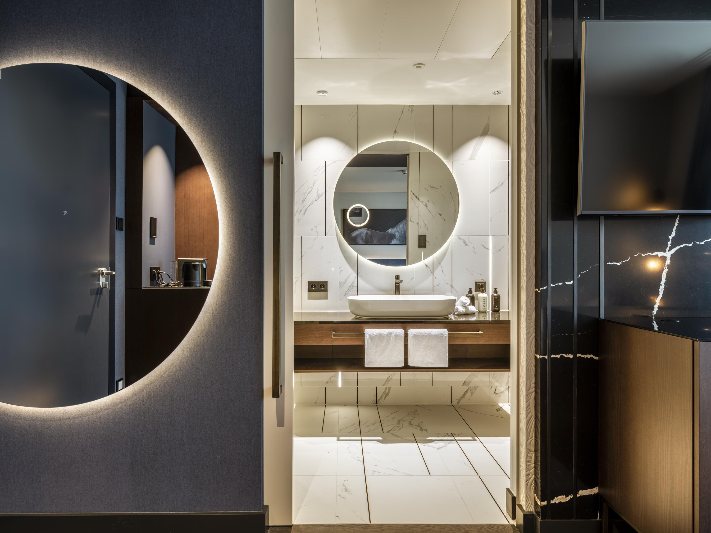 Une salle de bain moderne avec un grand miroir rond, un lavabo et un meuble-lavabo.