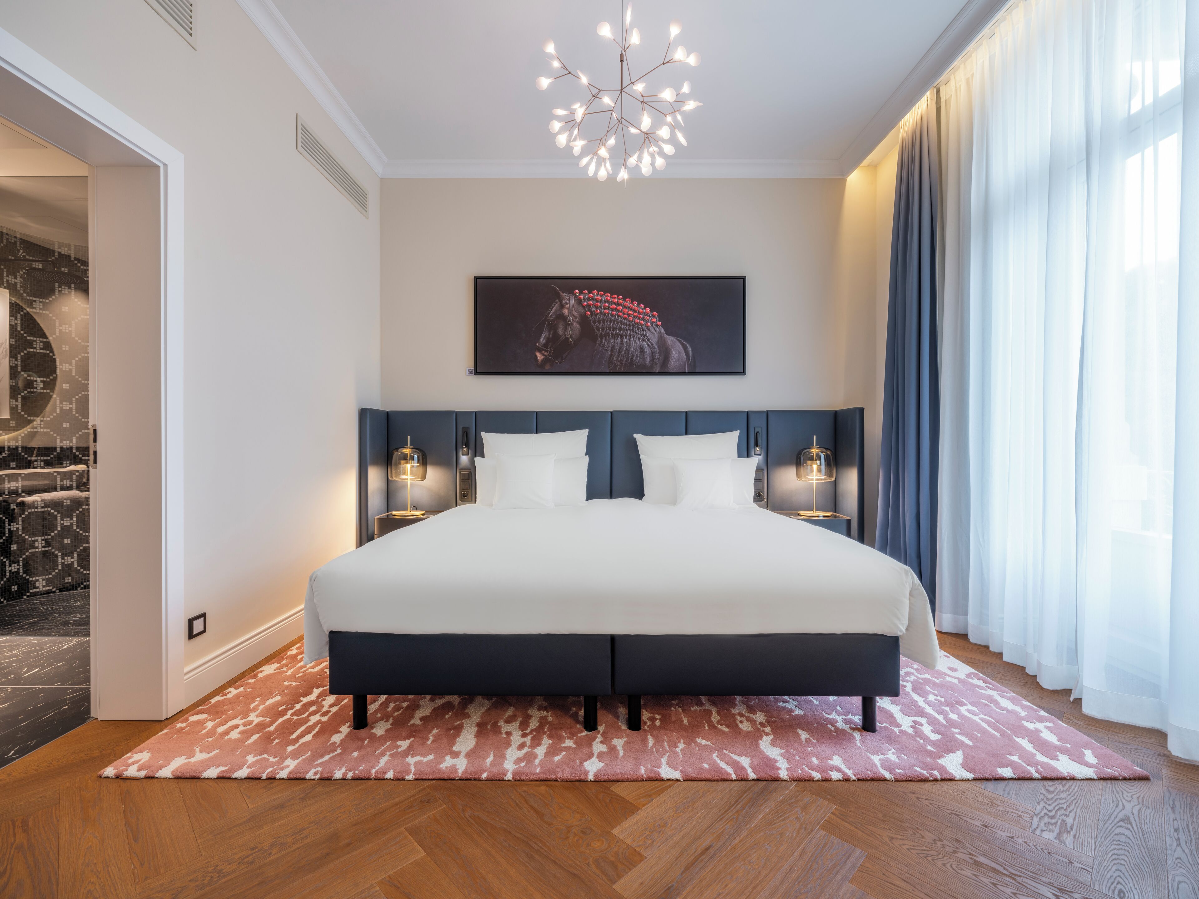 A modern bedroom with a large bed, a stone fireplace, and a chandelier.