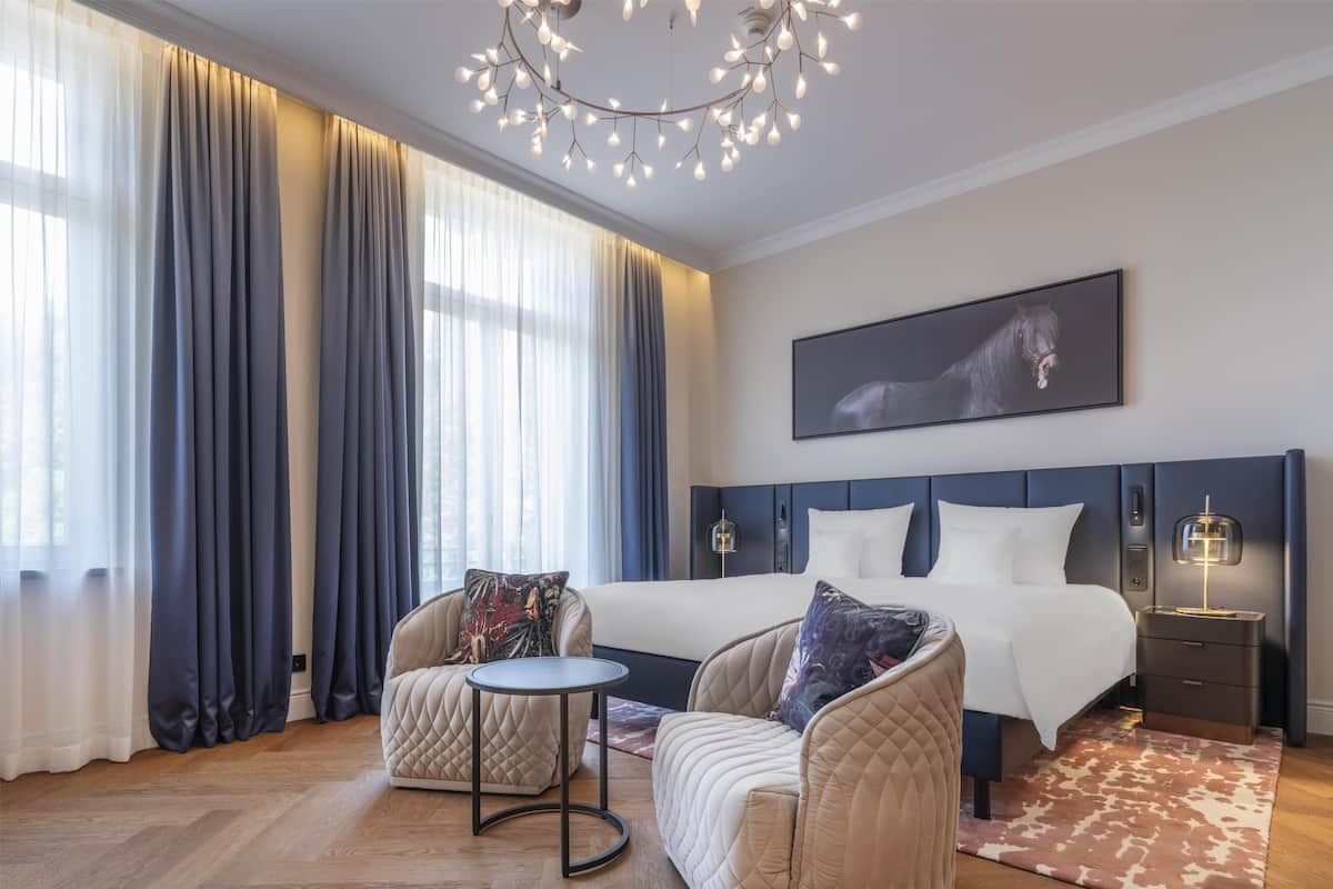 Une chambre à coucher moderne avec un grand lit, deux fauteuils, une petite table et un lustre.