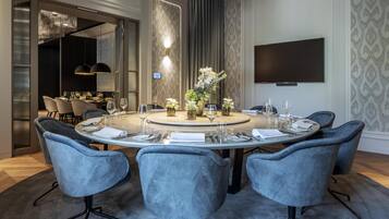 Un coin repas moderne avec une table ronde dressée pour six personnes, entourée de six chaises grises à revêtement rembourré. Un vase rempli de fleurs est placé au centre de la table.