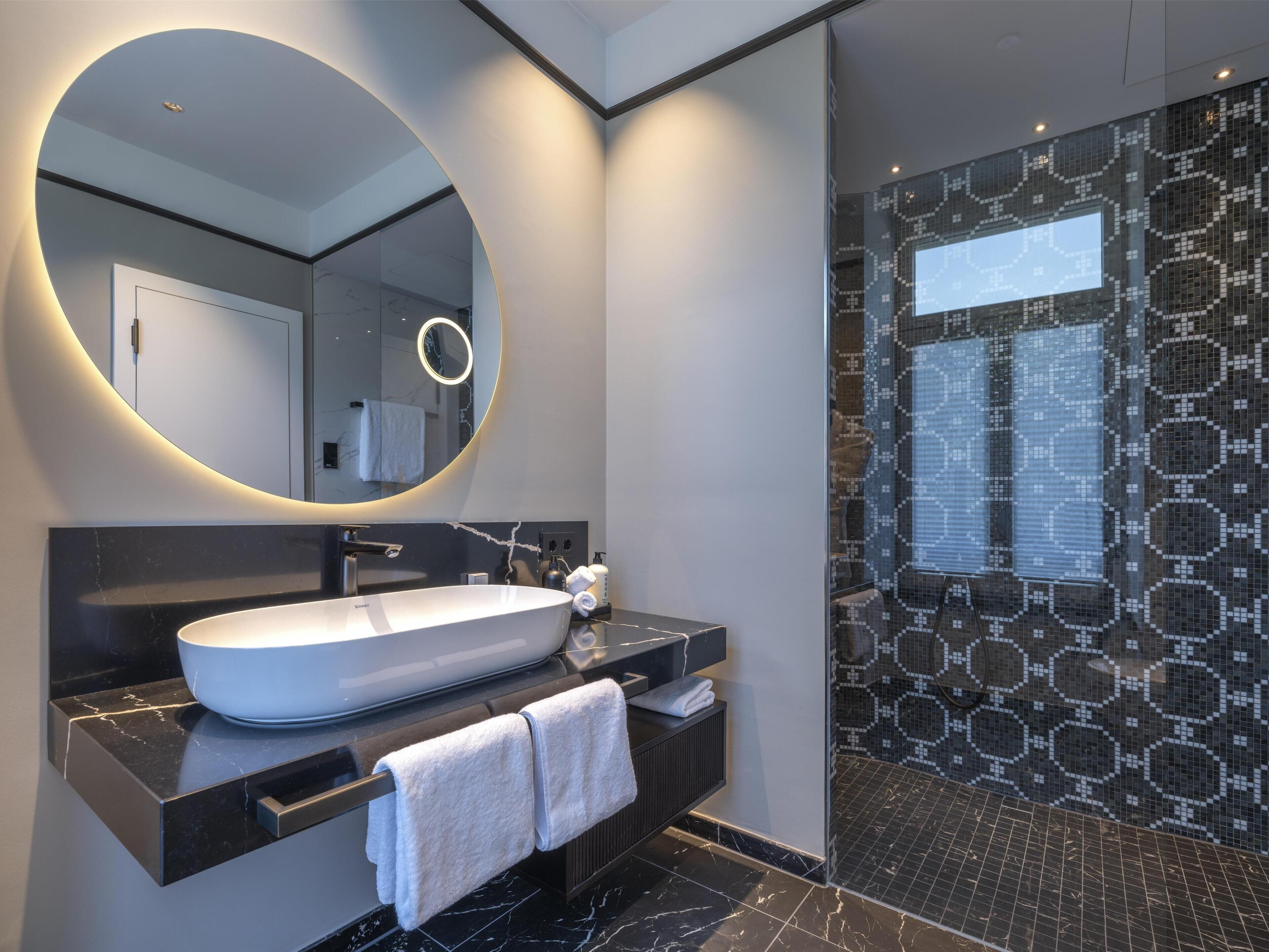 A modern bathroom with a large oval mirror, a white vessel sink, and a black countertop.