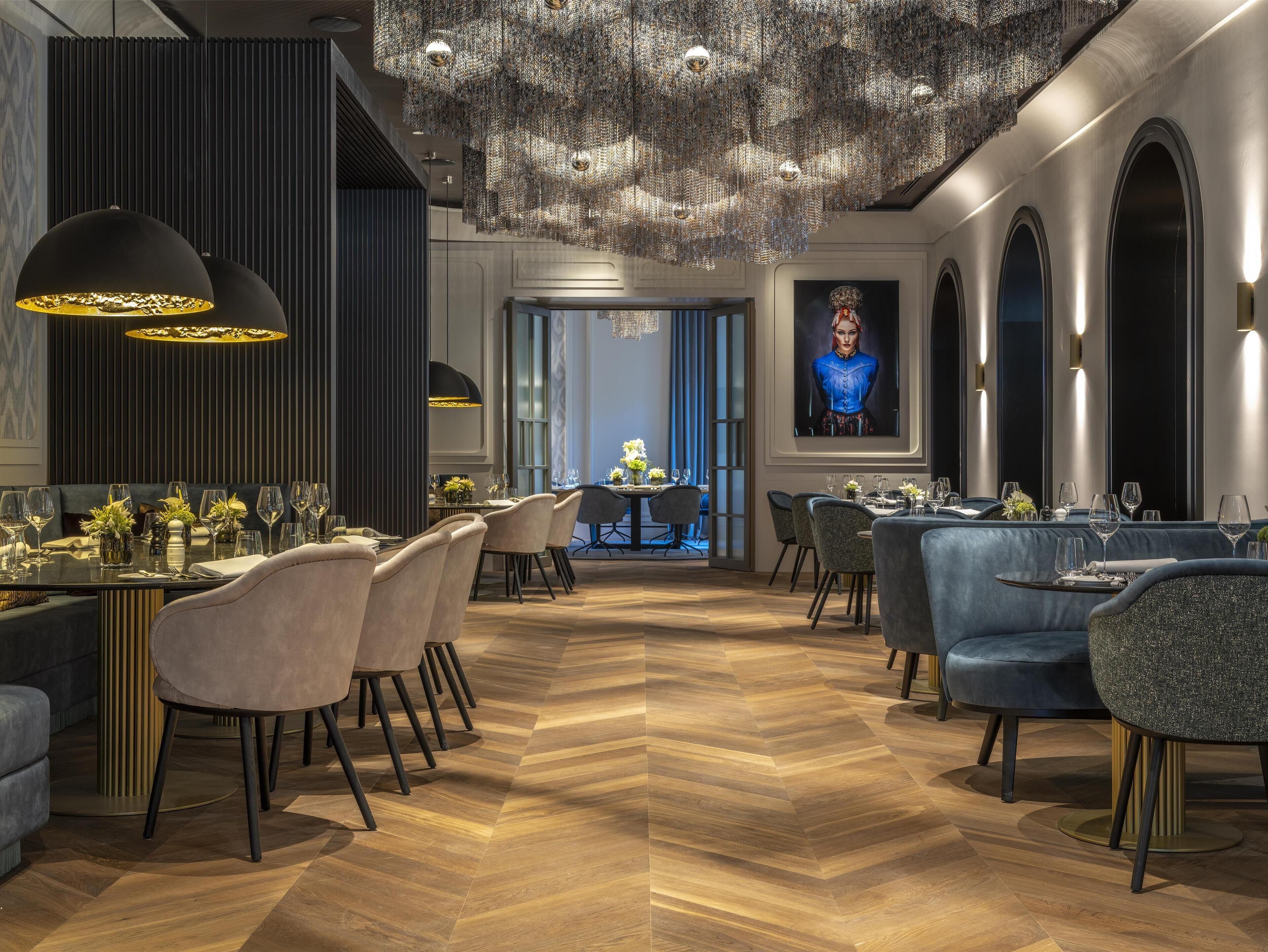 Un interior de restaurante moderno con suelo de madera en patrón de espiga, asientos mullidos y una araña.