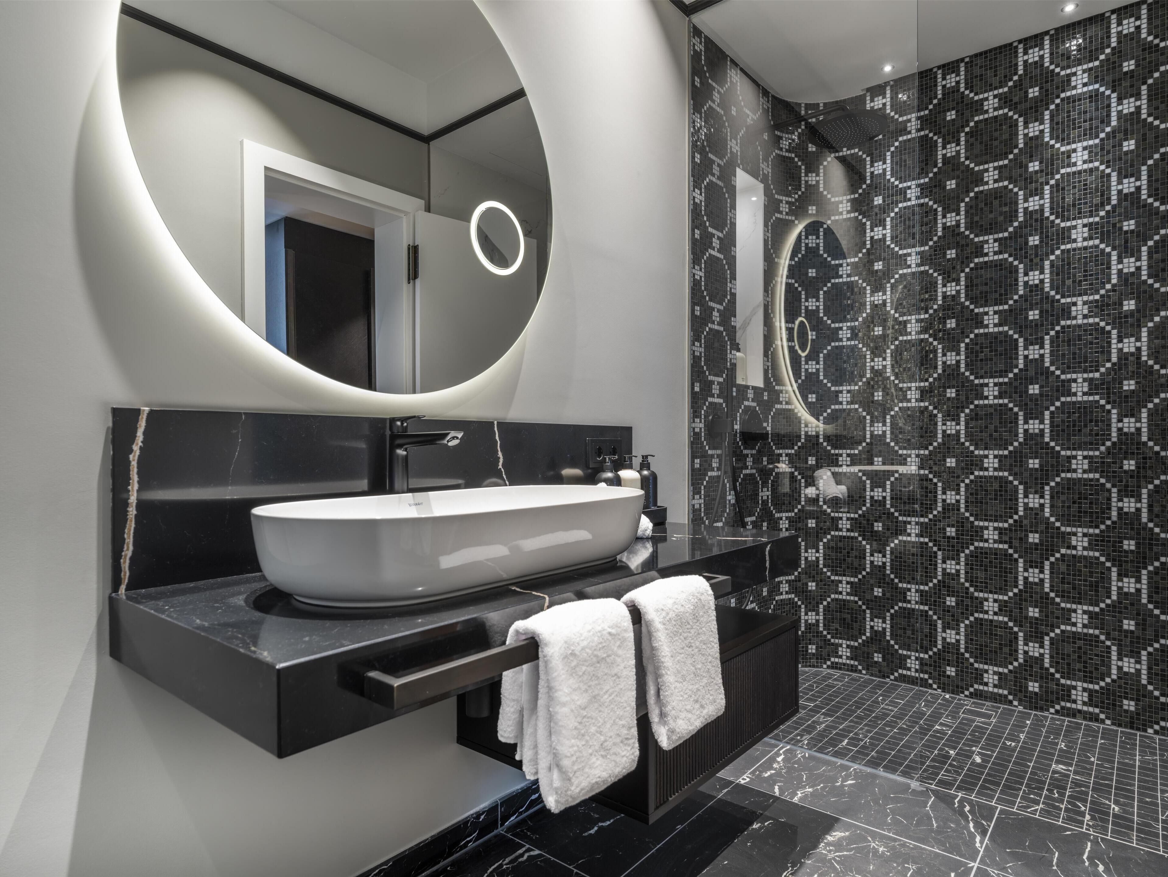 Un baño moderno con un espejo ovalado grande, un lavabo sobre encimera y un piso de baldosas negras.
