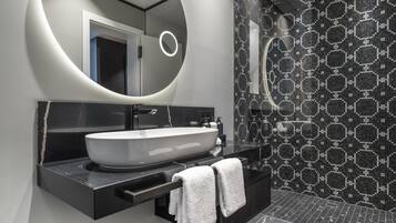 Un baño moderno con un espejo ovalado grande, un lavabo sobre encimera y un piso de baldosas negras.