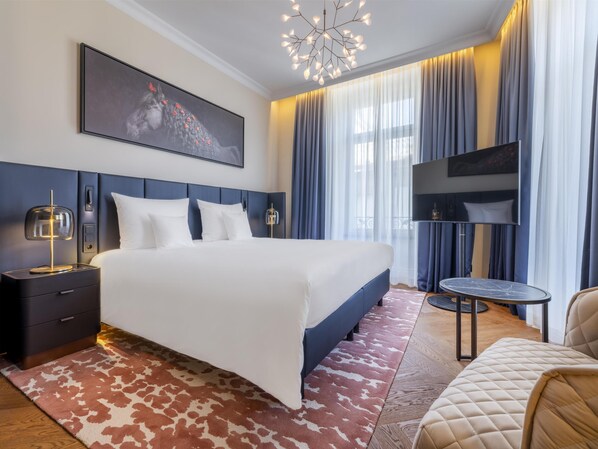 A modern hotel room with a large bed, a flat-screen TV, a desk, and a chair.