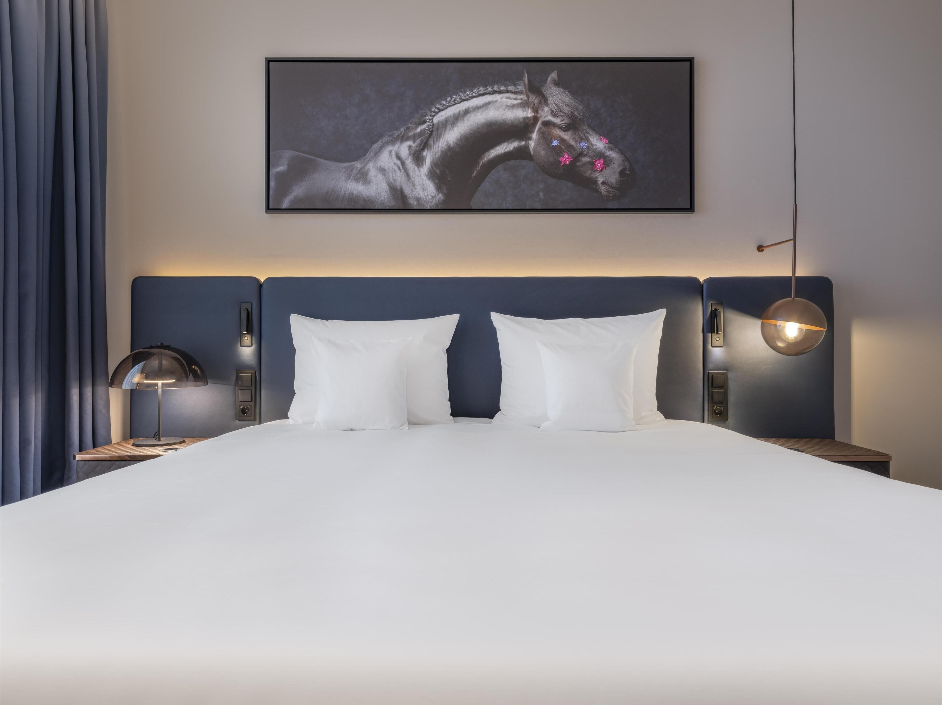 Ein modernes Hotelzimmer mit einem großen Bett, zwei Nachttischen, einem Wandbild eines Pferdes und einer Wandlampe.
