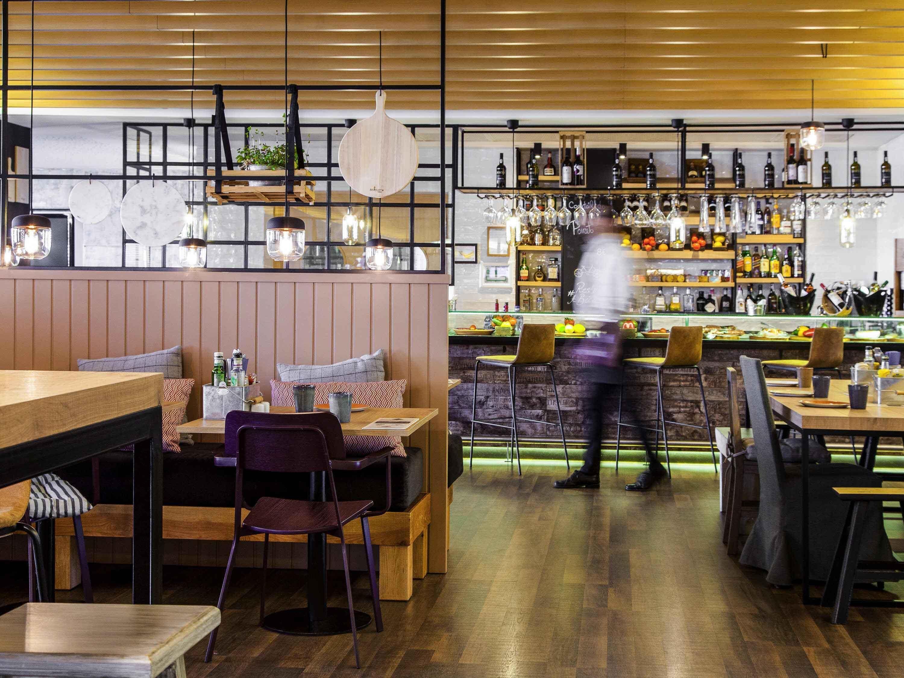 Ein Restaurant mit Holztischen, hängenden Lampen und einer Bar mit Flaschen und Gläsern.