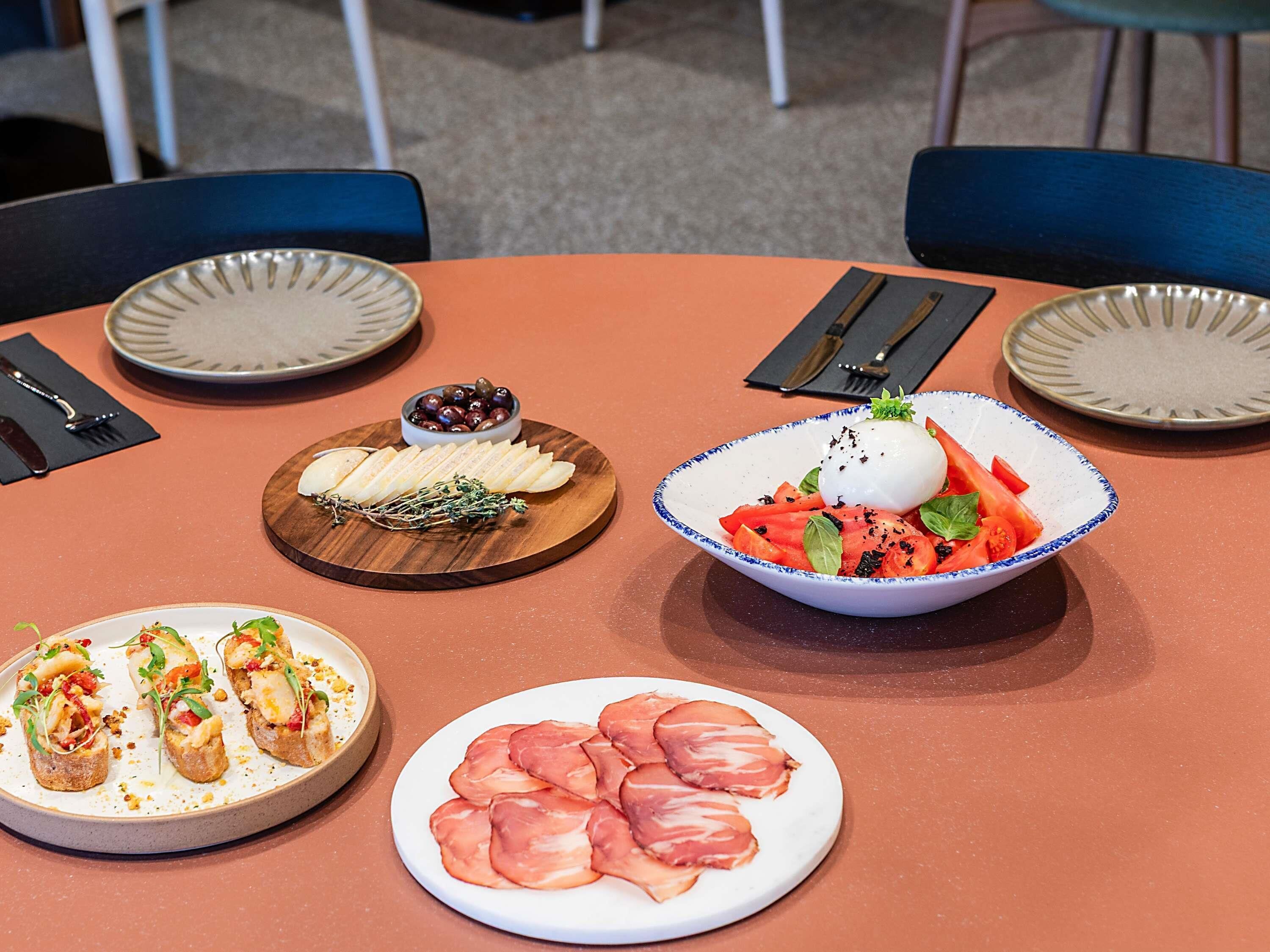 A round table with plates of food, cutlery, and napkins.