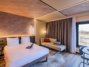 Ein modernes Hotelzimmer mit Bett, Sofa, Schreibtisch und Blick auf die Stadt.