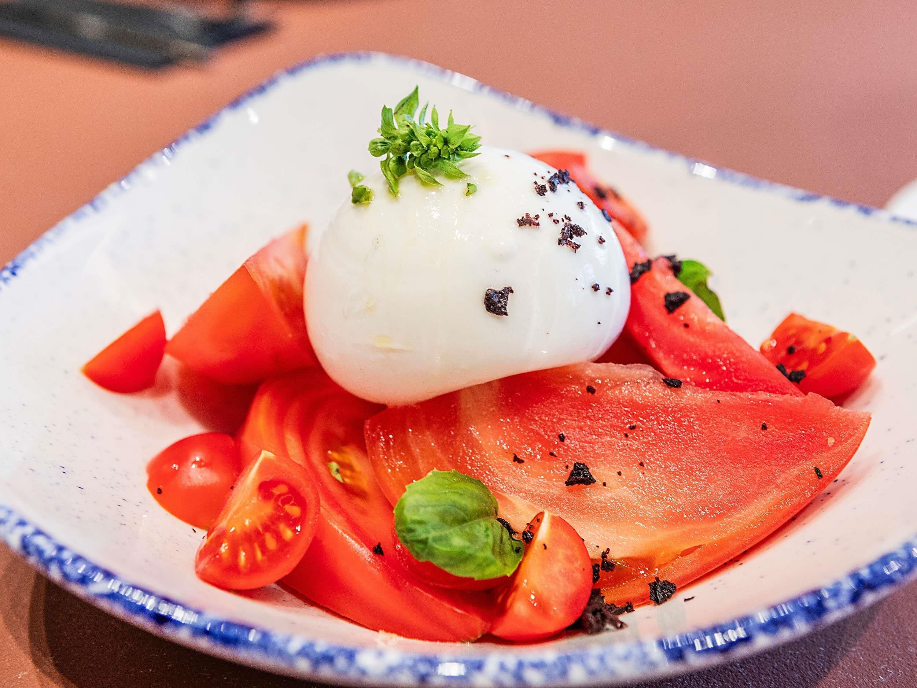 Ein Teller mit einer weißen, kugelförmigen Speise, Tomatenscheiben und einem Basilikumblatt.