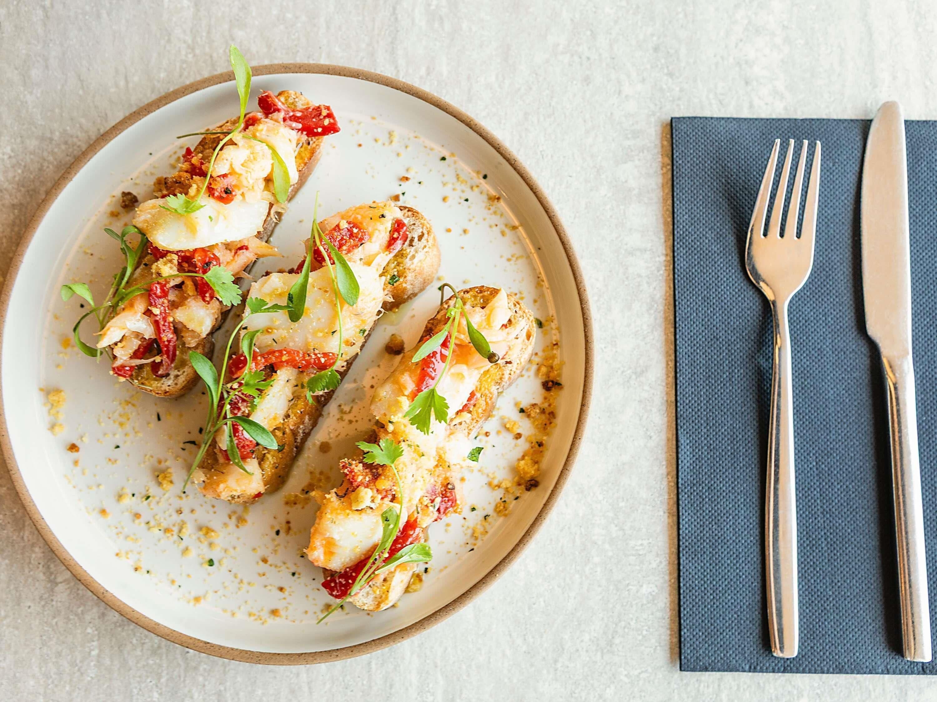 A plate with food items, a fork, and a knife on a napkin.