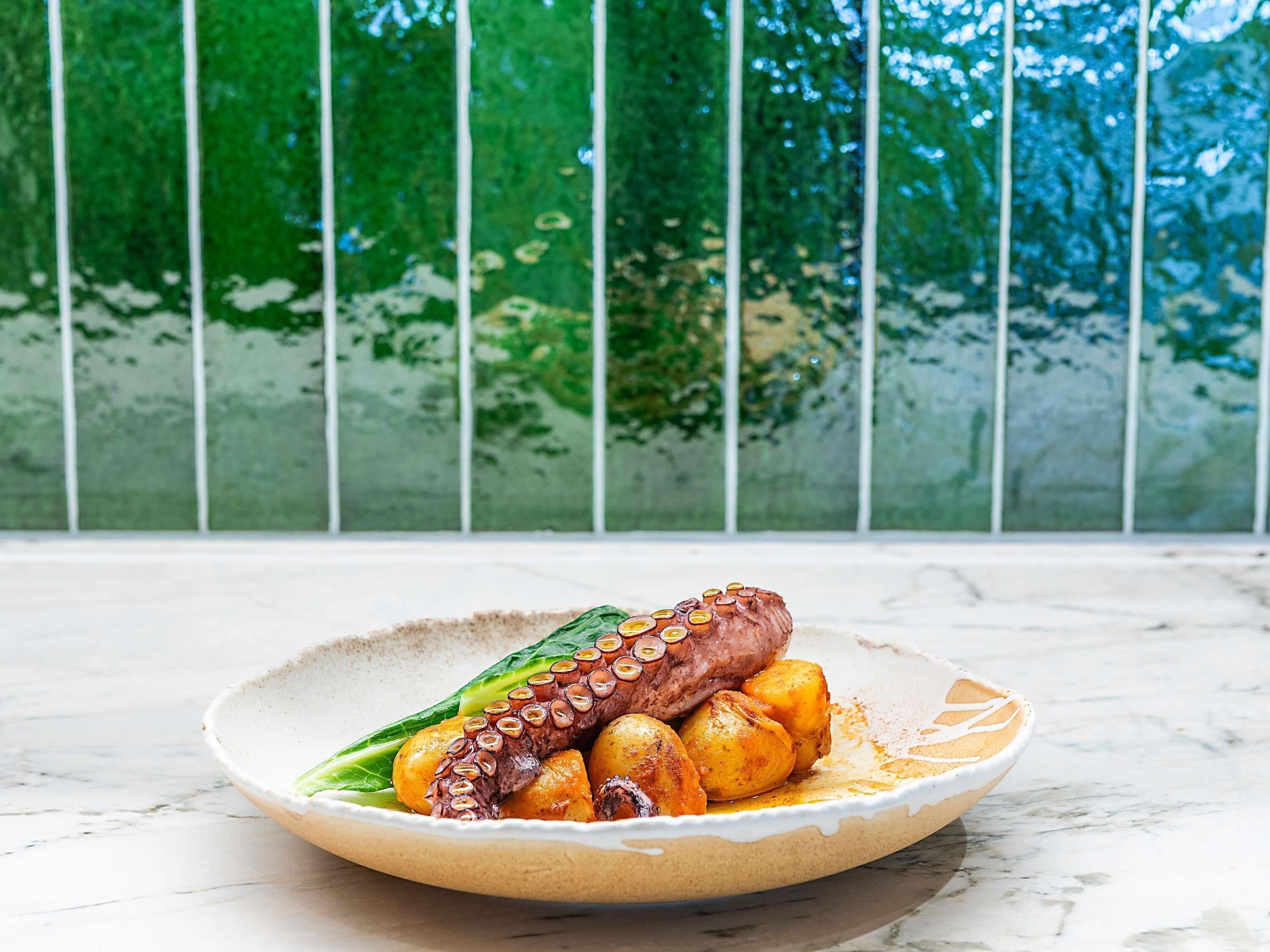 Ein Teller Essen auf einer Marmorplatte, dazu ein grünes Blattgemüse und Bratkartoffeln.