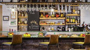 A bar area with hanging glasses, shelves with bottles, and a sign reading 'Pizzotto #Restaurant A Bicycleta.' - Novotel Lisboa (Lisbon)