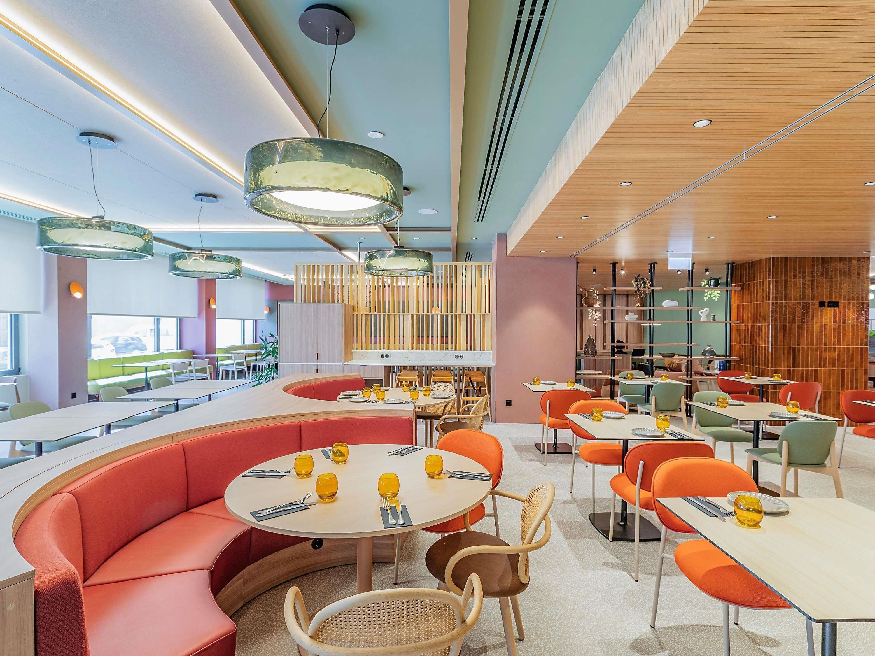 A modern restaurant interior with round tables, orange seating, and pendant lighting.