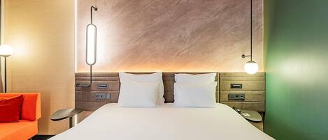 Una camera d'albergo con un letto grande, un comodino, una scrivania e un divano rosso.