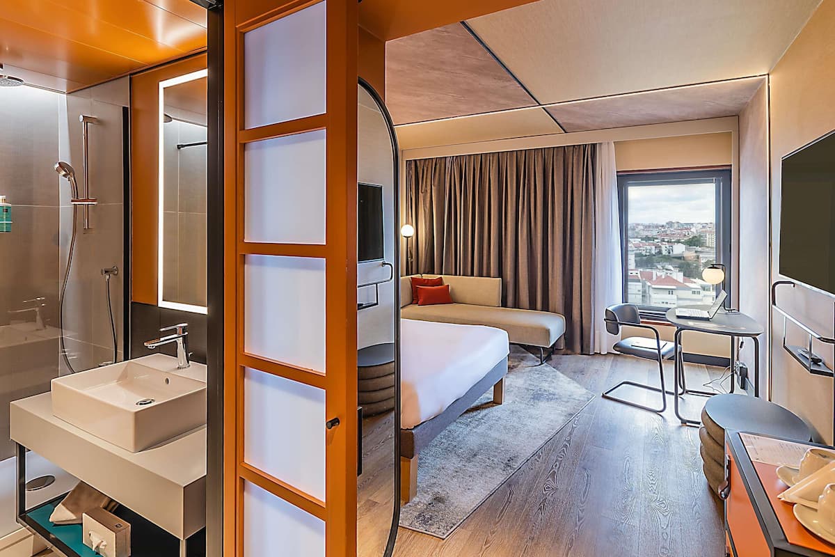 Ein Hotelzimmer mit Bad, einem Bett, einem Schreibtisch und Blick auf die Stadt.