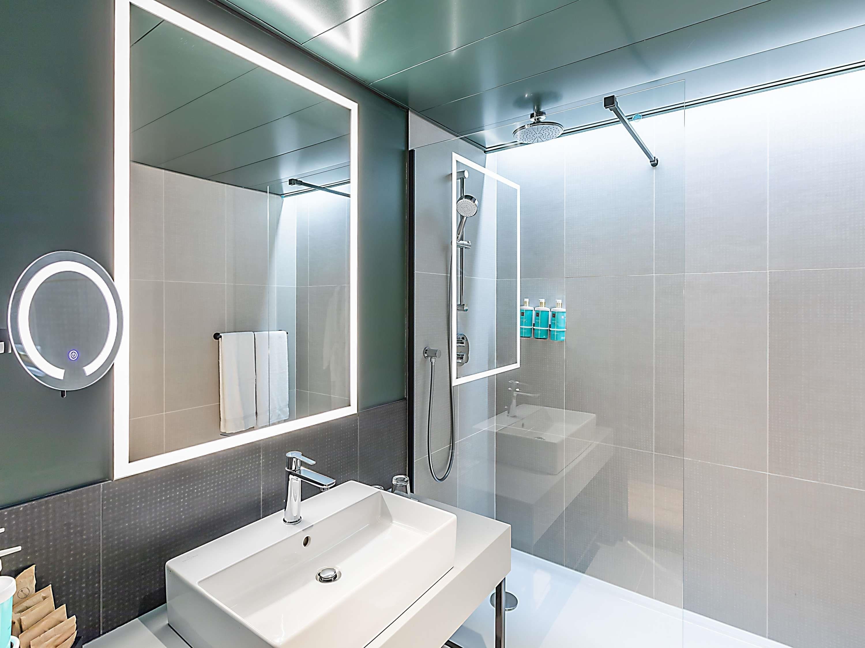 A modern bathroom with a large mirror, a sink, and a shower.