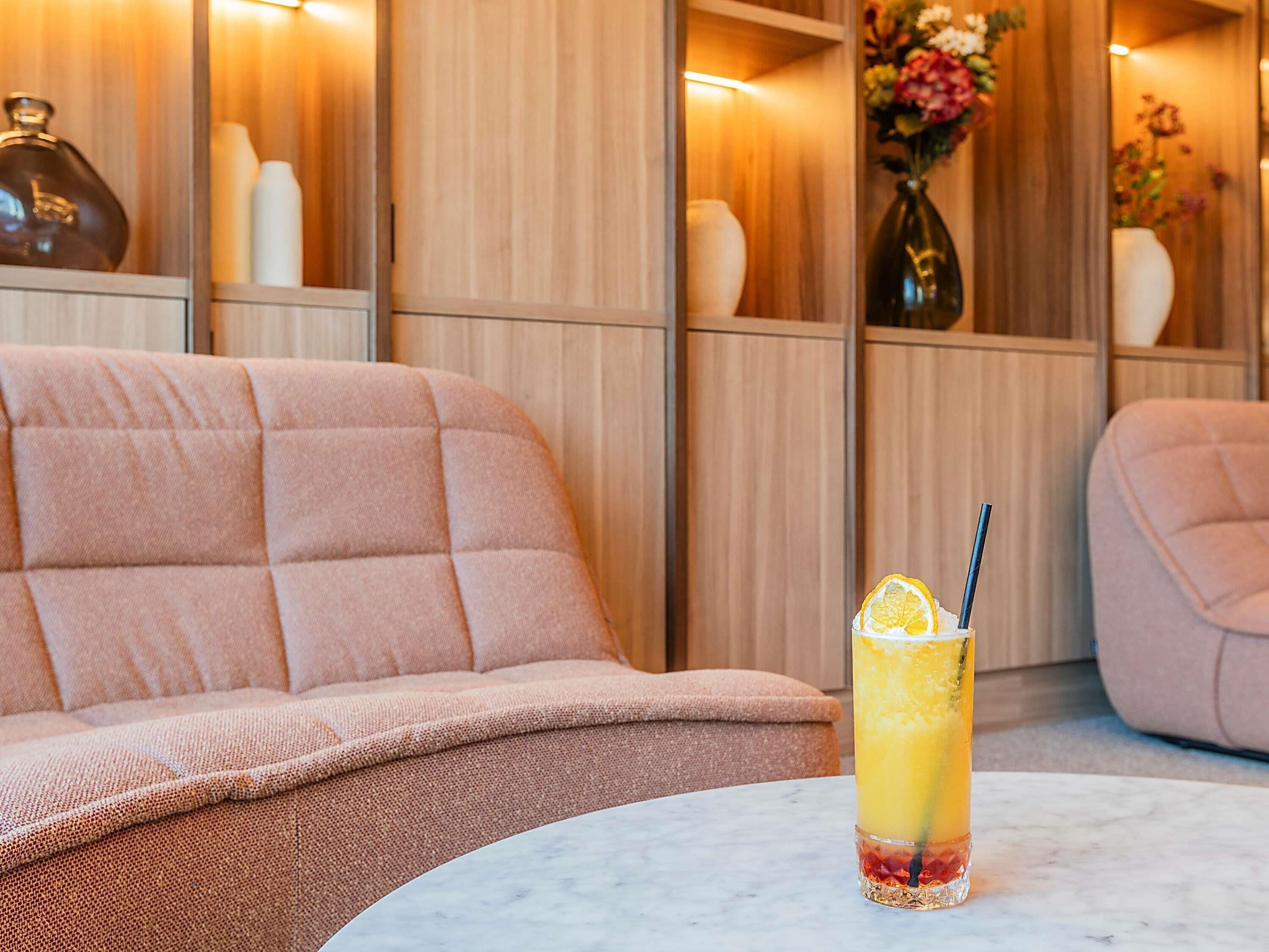 Een zithoek met een comfortabele bank en een tafel met een glas geel drankje.