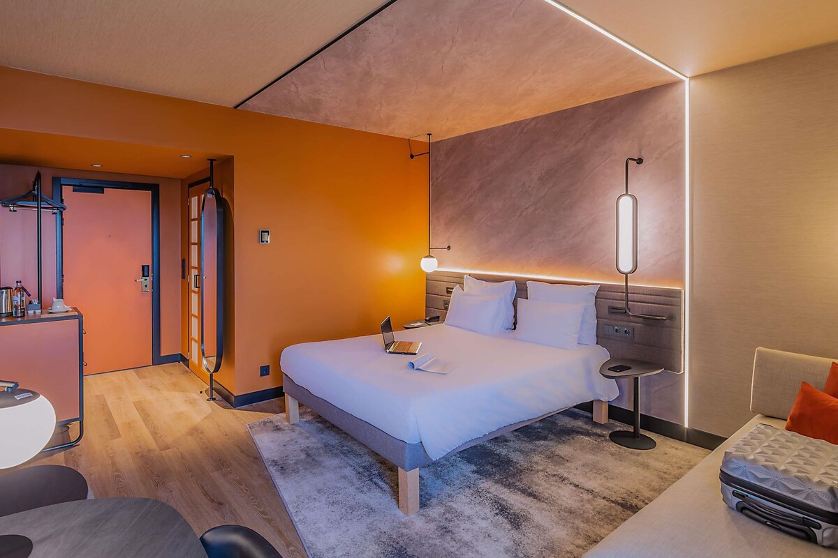 A modern hotel room with a large bed, bedside tables, a desk, and a chair.
