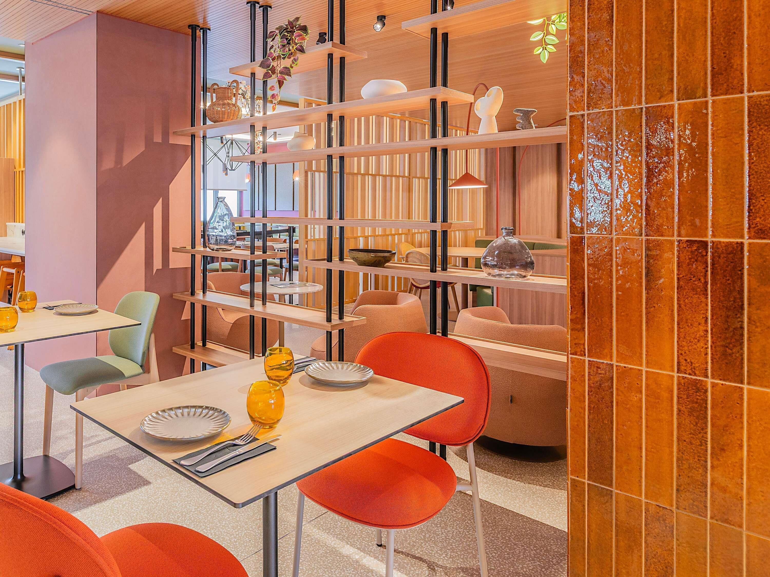 Ein modernes Interieur mit Essbereich, der Tische und Stühle umfasst, einem dekorativen Regal mit verschiedenen Gegenständen sowie einer Wand mit einem einzigartigen Fliesenmuster.